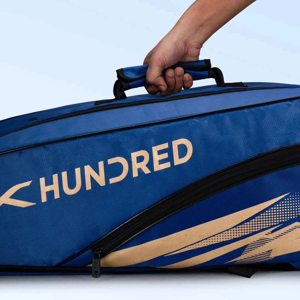 HUNDRED Cosmogear Kit Bag in blue textured fabric with black zippers, peach-gold branding and sweeping graphic accents