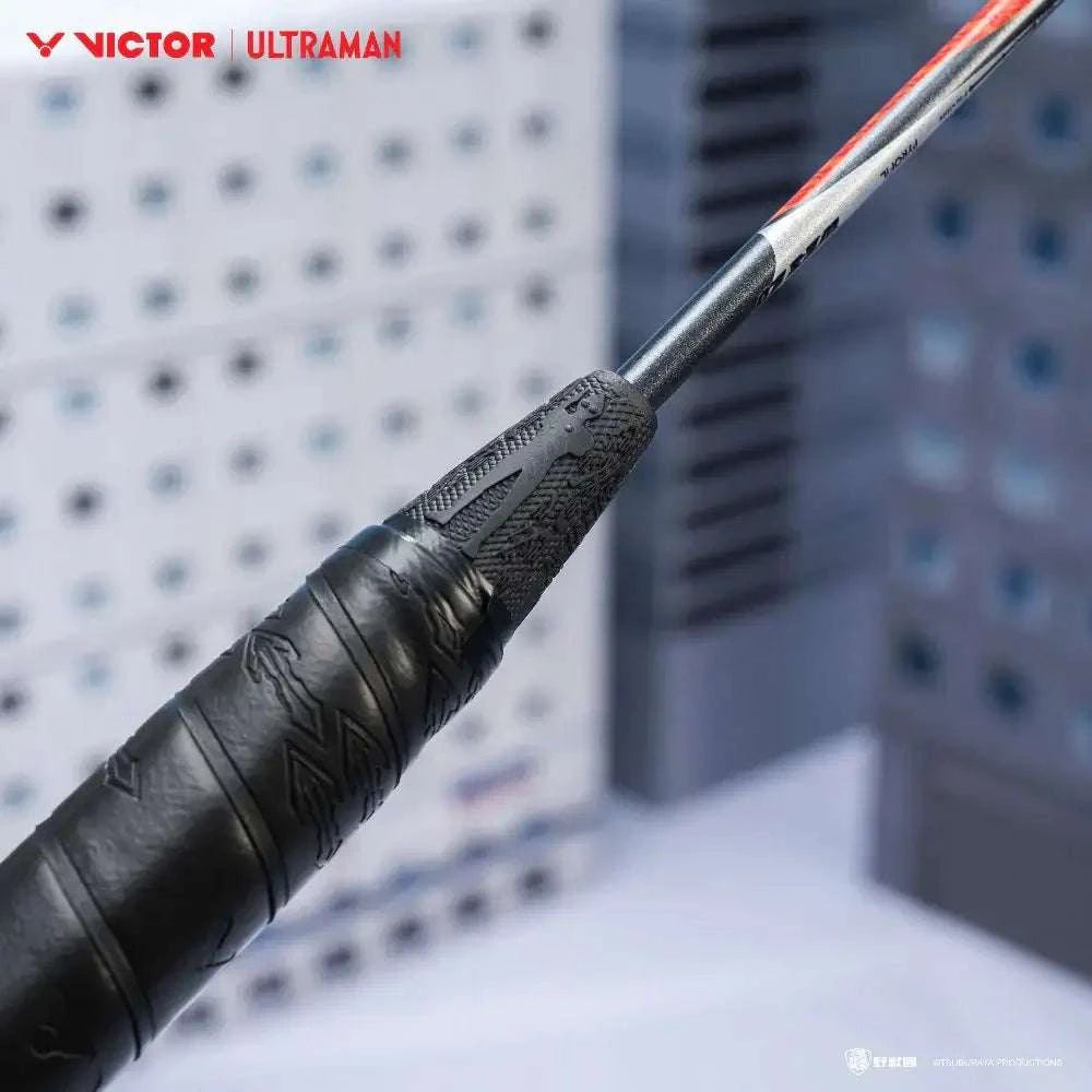 Badminton racket from the VICTOR X ULTRAMAN Collection with a black textured grip and silver shaft with red accents