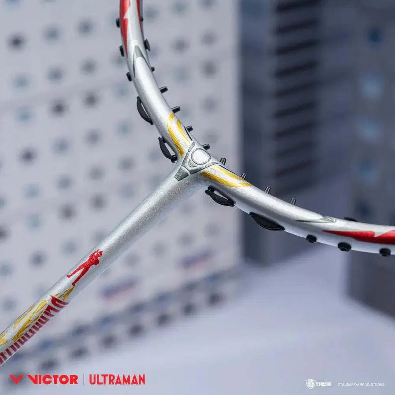 Badminton racket from the VICTOR X ULTRAMAN Collection with a silver frame, red and yellow accents, and Ultraman graphics.