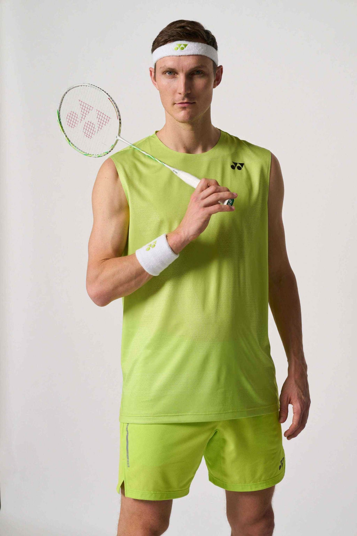 Yonex Astrox 100ZZ VA badminton racket held by a player in a neon lime sleeveless outfit, with green frame