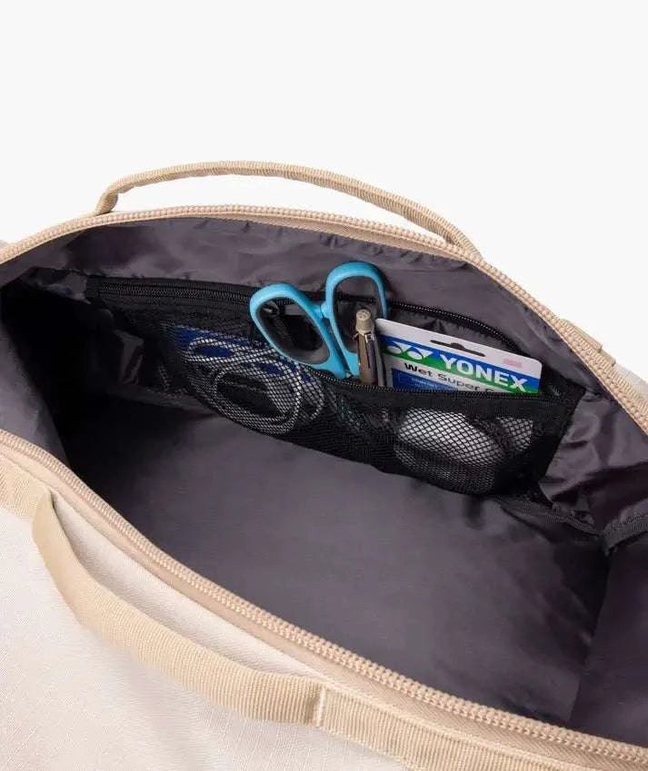Yonex GEARLOGIC Backpack with a beige fabric exterior, wide zippered opening and black mesh interior pockets holding accessories